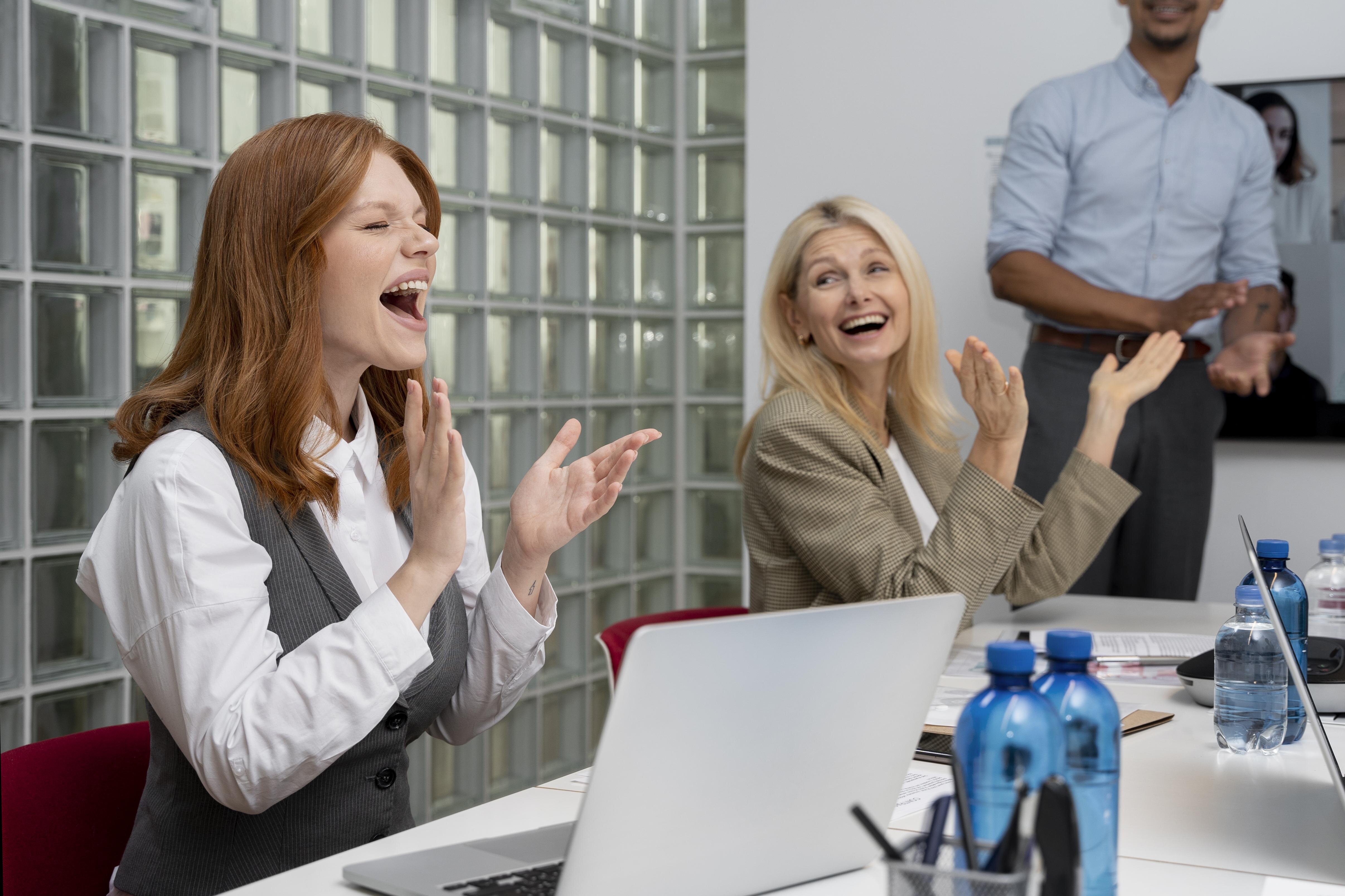 Three employees applaud during a meeting in a modern office